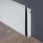 Witte plint tegen grijze muur en houten vloer.