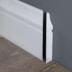 Witte plint met decoratieve rand tegen grijze muur.