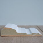 Profiel van wit houten plint op houten vloer.