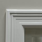 Wit geschilderde houten deurlijst op beige muur.