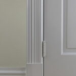 Wit deurscharnier op houten vloer en muur.