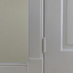 Witte deur met scharnier en plint op houten vloer.