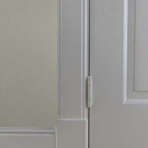 Witte deur met scharnier en plint op houten vloer.