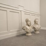 Twee beeldhouwwerken in lege kamer op vloer.