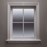 Wit kozijn met vierdelig raam tegen grijze muur.
