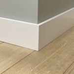 Witte plint op houten vloer, hoek zicht.