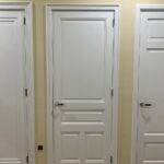 Drie witte deuren in een gang met houten vloer.