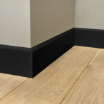 Zwarte plint tegen houten vloer en witte muurhoek.