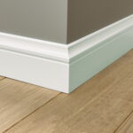 Laminaatvloer met witte plint tegen grijze muurhoek.