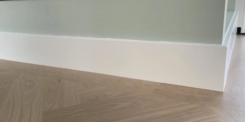 Strak wit geschilderde MDF plint op een visgraatvloer tegen een lichtgroene wand