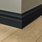 Zwarte plint op houten vloer bij muurhoek.
