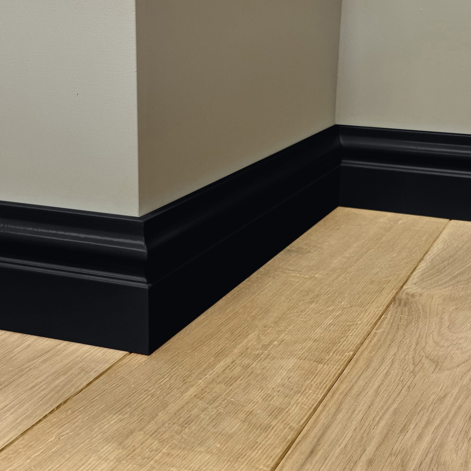 Witte muur met zwarte plint en houten vloer