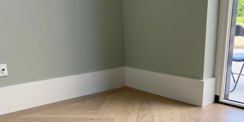 Strak witte plinten in een hoek met een nette verstekaansluiting op een visgraatvloer