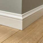 Witte mdf plint langs houten vloer en muurhoek.