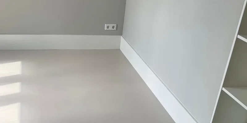 Strakke witte plint in een lichte, rustige ruimte met grijze muren en een gladde vloer