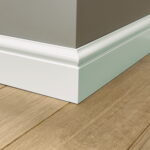 Wit geschilderde plint tegen houten vloer en beige muur.