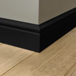Zwarte plint langs houten vloer en witte muur.