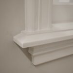 Witte vensterbank met klassieke details op grijze muur.