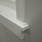 Witte houten raamkozijnhoek gedetailleerd tegen grijze muur.