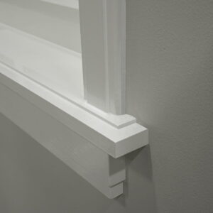 Witte houten raamkozijnhoek gedetailleerd tegen grijze muur.