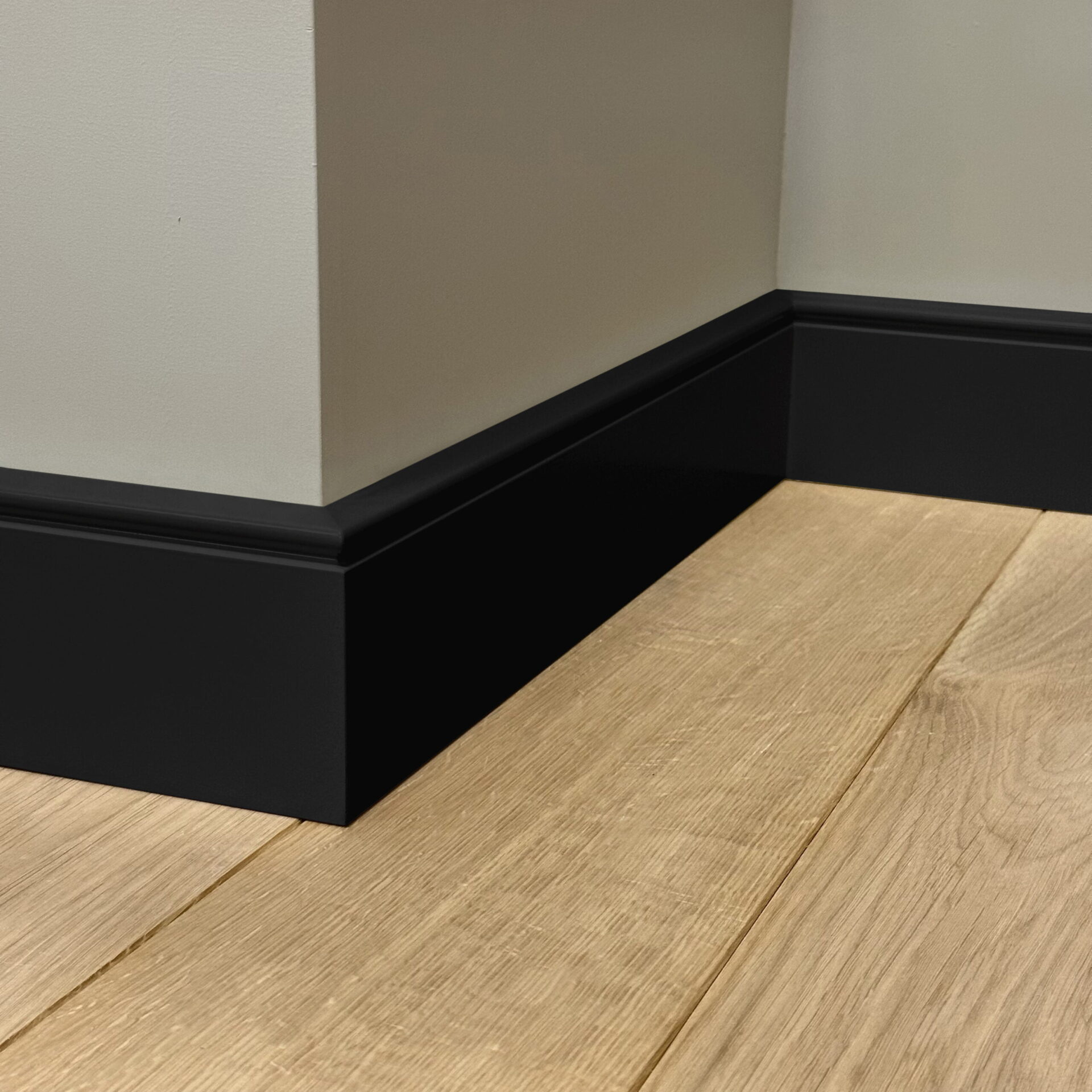 Hoek muur met zwarte plint en houten vloer.