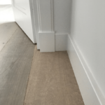 Houten vloer met witte plint en open deur.