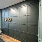 Donkergroene muur met houten lambrisering en decoratiestukken.