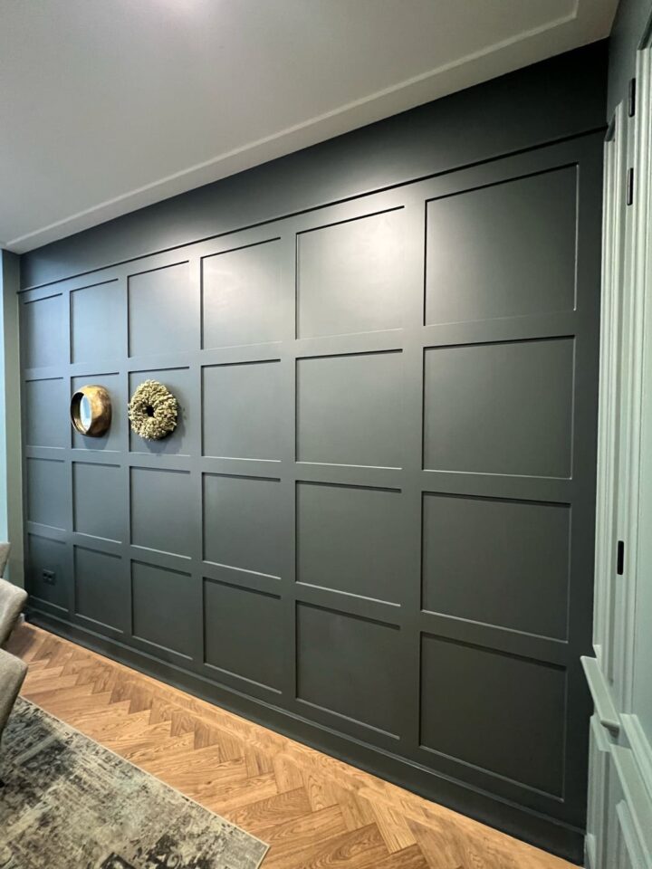 Donkergroene muur met houten lambrisering en decoratiestukken.