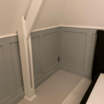 Zolderkamer met houten panelen en schuin raam.