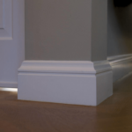 Witte plint tegen grijze muur op houten vloer.