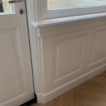 Witte houten deur en lambrisering in hoek.