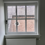 Uitzicht op bakstenen gebouw door raam met radiator